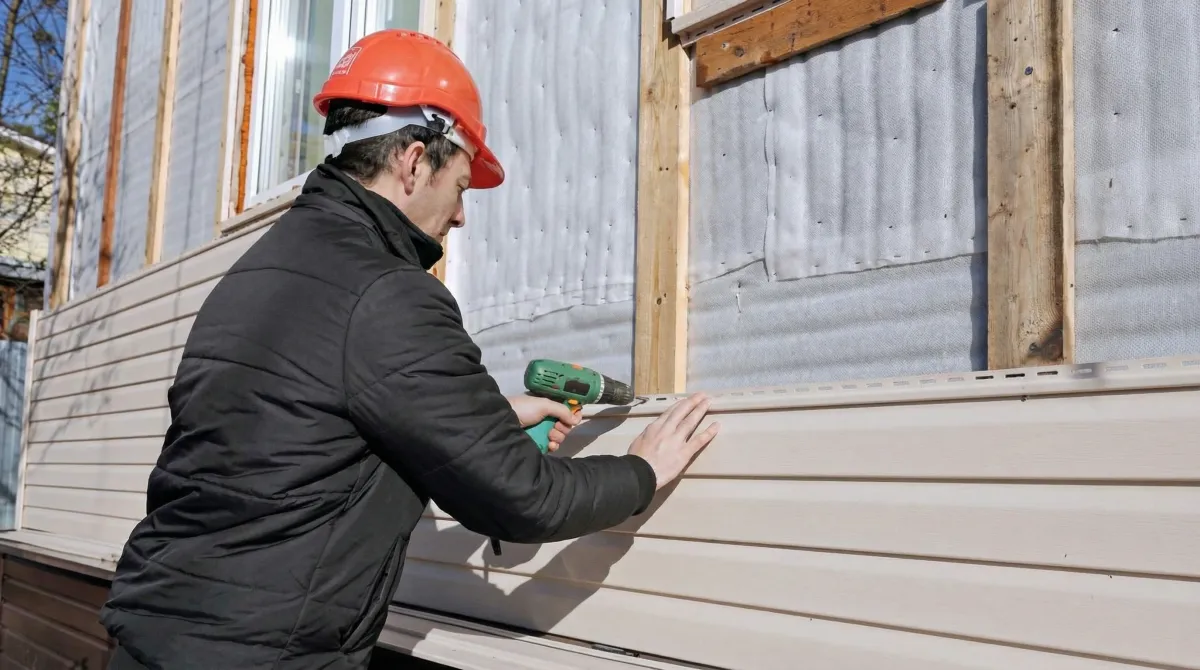 Siding replacement professional using a power drill to install new tan vinyl siding on a home exterior in Cambridge, MA